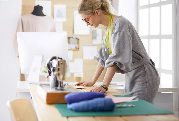 Neue modische Stile schaffen. Fröhliche junge Frau näht, während sie an ihrem Arbeitsplatz in der Modewerkstatt sitzt — Stockfoto