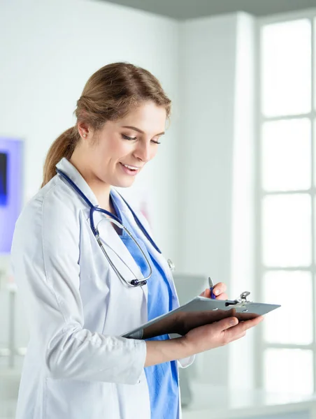 Doktor se stetoskopem se zápisníkem v ruce. Detailní záběr ženského lékaře vyplňující lékařskou formu ve schránce, zatímco stojí rovně v nemocnici — Stock fotografie