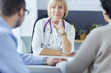 İlgili kıdemli doktor ofisinde yatan hastayı dinliyor.