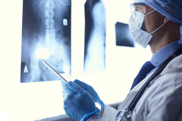 Médico en el hospital sentado en el escritorio mirando los rayos X en la tableta contra el fondo blanco con rayos X — Foto de Stock