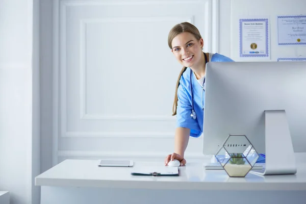 Portrait of female physician using laptop computer while standing near reception desk at clinic or emergency hospital