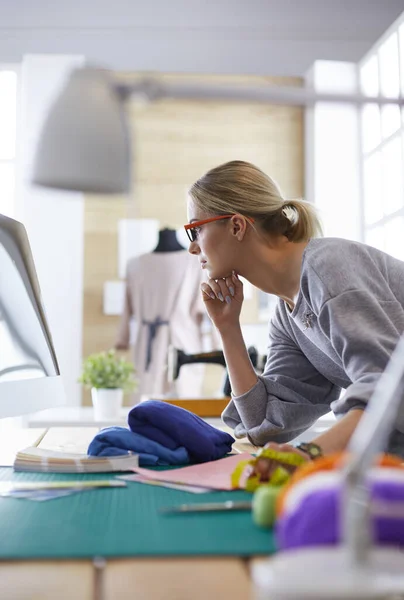 Unga attraktiva kvinnor modedesigner lutar sig mot kontorsbord, arbetar med en bärbar dator — Stockfoto