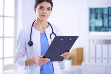 Doktor muayenehanesinde steteskopla gülümseyen genç bir bayan doktor.