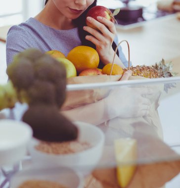 Gülümseyen kadın buzdolabından taze meyve alıyor, sağlıklı yiyecek konsepti.