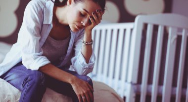 Yatakta çocuk karyolası yakın oturan genç yorgun kadın