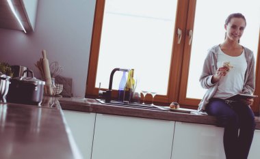 Mutfakta dijital tablet kullanan güzel genç bir kadın.