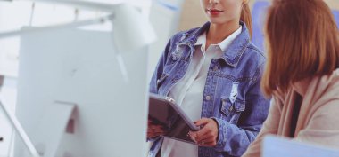 Masanın yanında duran iki genç kadın enstrüman, plan ve dizüstü bilgisayarla