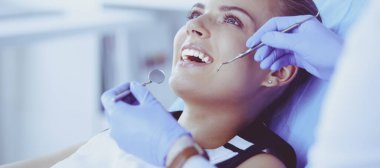 Dişçi muayenehanesinde diş muayenesi yapan ağzı açık genç bir kadın hasta..