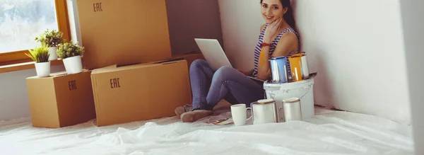 Ritratto di giovane donna mentre dipinge un nuovo appartamento, seduta con computer portatile — Foto Stock