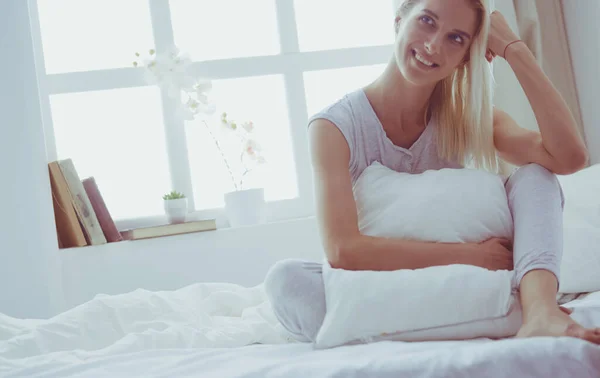 Roztomilá žena drží polštář při sezení na posteli — Stock fotografie