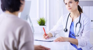 Doktor ve hasta hastane danışma odasında tıbbi sorunları tartışıyorlar. Doktor hasta formunu dolduruyor.