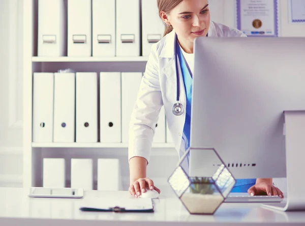 Portrait of female physician using laptop computer while standing near reception desk at clinic or emergency hospital