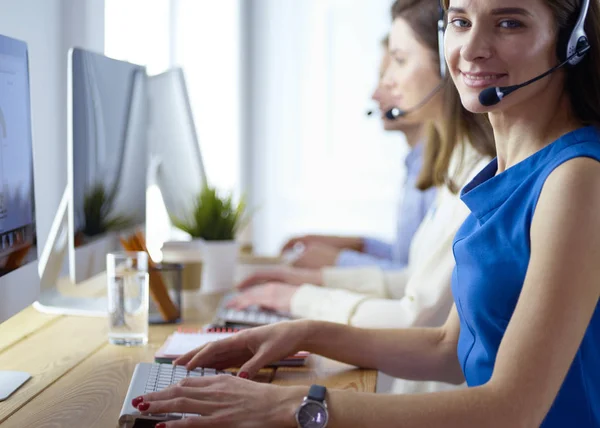 Porträt eines jungen Callcenter-Betreibers mit Headset und Kollegen, die im Hintergrund im Büro arbeiten — Stockfoto