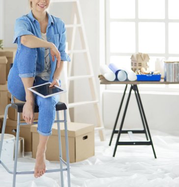 Genç bir kadın evde oturuyor ve tablet bilgisayar kullanarak internetten yeni mobilyalar alıyor.