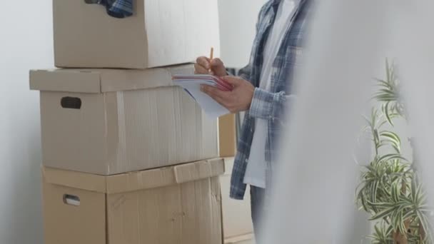 Um homem em movimento de pé em apartamento vazio, Entre as Caixas, Verificando a Lista de Coisas — Vídeo de Stock