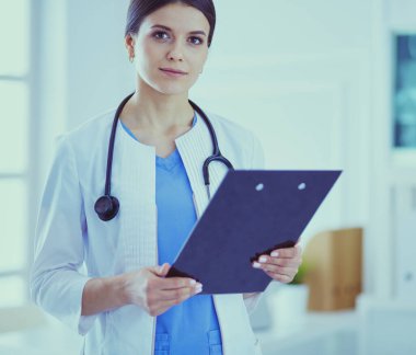 Doktor muayenehanesinde steteskopla gülümseyen genç bir bayan doktor.