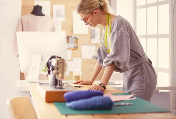 Crear nuevos estilos de moda. Joven alegre cosiendo mientras está sentada en su lugar de trabajo en el taller de moda — Foto de Stock