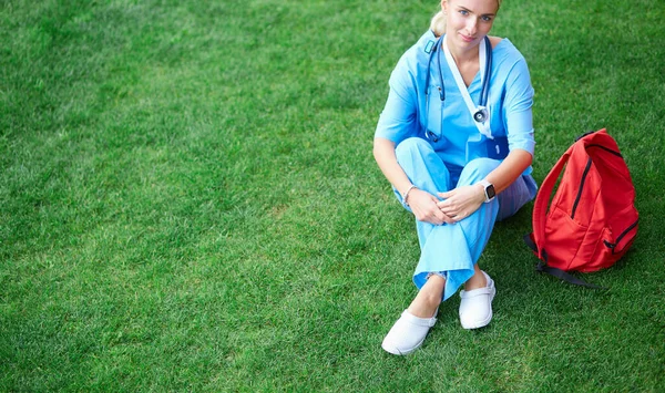 Porträtt av kvinnlig läkare sitter på gräs — Stockfoto