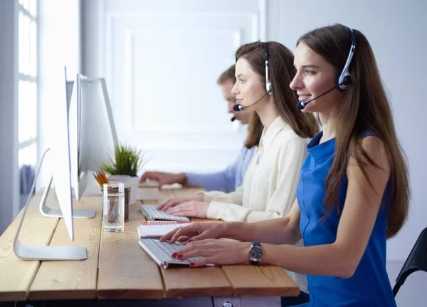 Retrato de jovem operador de call center usando fone de ouvido com colegas trabalhando em segundo plano no escritório — Fotografia de Stock