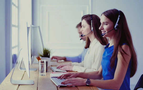 Porträt eines jungen Callcenter-Betreibers mit Headset und Kollegen, die im Hintergrund im Büro arbeiten — Stockfoto