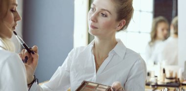 Makyöz, genç bir kadının profesyonel makyajını yapıyor.