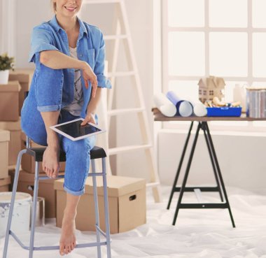 Genç bir kadın evde oturuyor ve tablet bilgisayar kullanarak internetten yeni mobilyalar alıyor.