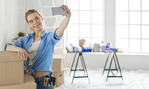 Joyeux jeune femme prenant selfie tout en souriant joyeusement, après avoir emménagé dans un nouvel appartement — Photo