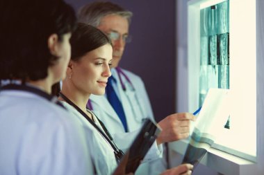 Bir grup doktor bir klinikte röntgenleri inceliyor, teşhis koymayı düşünüyorlar.