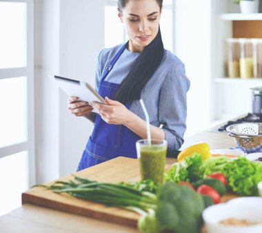 Mutfakta yemek yapmak için tablet bilgisayar kullanan genç bir kadın.