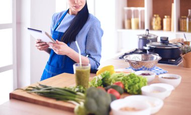 Mutfakta yemek yapmak için tablet bilgisayar kullanan genç bir kadın.