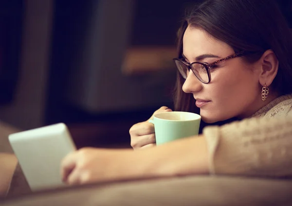 Donna seduta sul tappeto vicino al divano con una tavoletta, bere caffè da una tazza. Concetto di educazione online . — Foto Stock