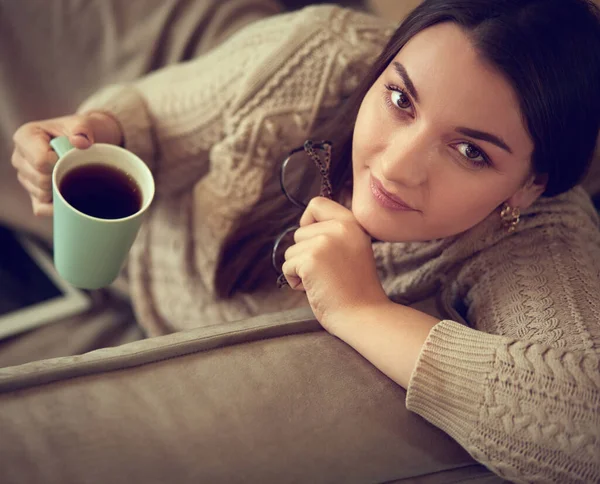 Kobieta w domu ubrania siedzi na dywanie w pobliżu kanapy za pomocą tabletu, pijąc kawę z zielonej filiżanki — Zdjęcie stockowe