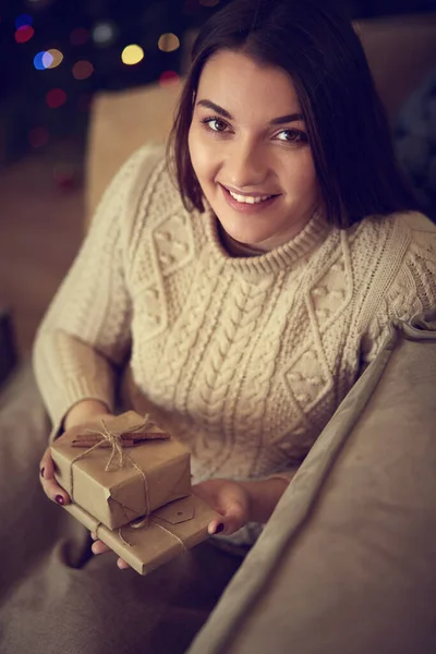 Young woman opening present on sofa at home — Stock Photo, Image