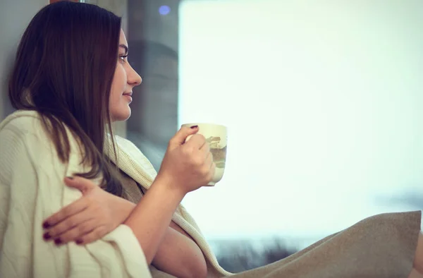 Jonge vrouw in plaid met kop hete thee zitten op de vensterbank — Stockfoto