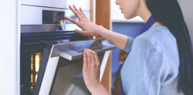 Güzel genç bayan pastasının fırında ne yaptığını kontrol ediyor.