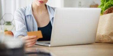 Mutfakta bilgisayar ve kredi kartı kullanan gülümseyen bir kadın.