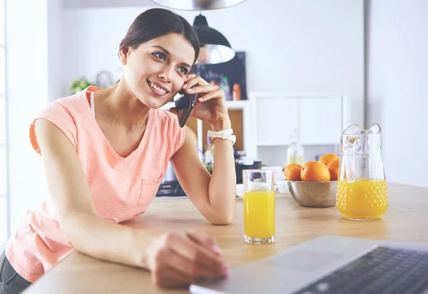 Ung kvinna i köket med bärbar dator ser recept, leende. Begreppet livsmedelsbloggare — Stockfoto