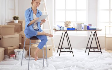 Genç bir kadın evde oturuyor ve tablet bilgisayar kullanarak internetten yeni mobilyalar alıyor.