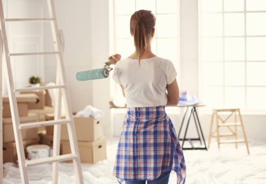 Güzel gülümseyen kadın evin iç duvarını boya ile boyuyor.