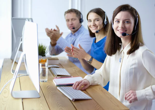 Retrato de jovem operador de call center usando fone de ouvido com colegas trabalhando em segundo plano no escritório — Fotografia de Stock