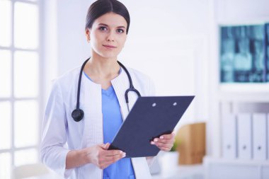 Doktor muayenehanesinde steteskopla gülümseyen genç bir bayan doktor.