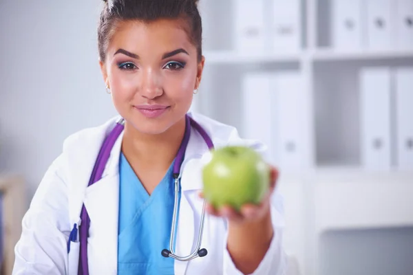Žena lékař ruka drží zelené jablko, sedí za stolem — Stock fotografie