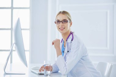 Hastanede masasında oturan genç bir kadın doktorun portresi.