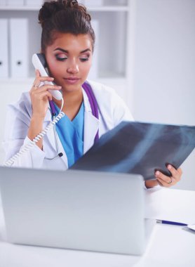 Röntgen taraması yapan kadın doktor teşhis merkezinde telefonla konuşuyor, masada oturuyor.