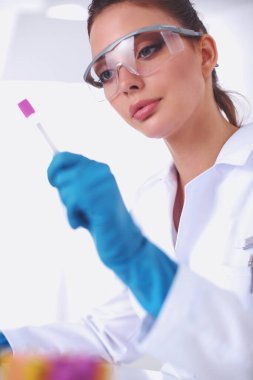 Kadın araştırmacı, beyaz arka planda izole edilmiş ilaç şişeleri ve mataralarla çevrili.