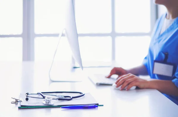 Schöne junge lächelnde Ärztin sitzt am Schreibtisch — Stockfoto