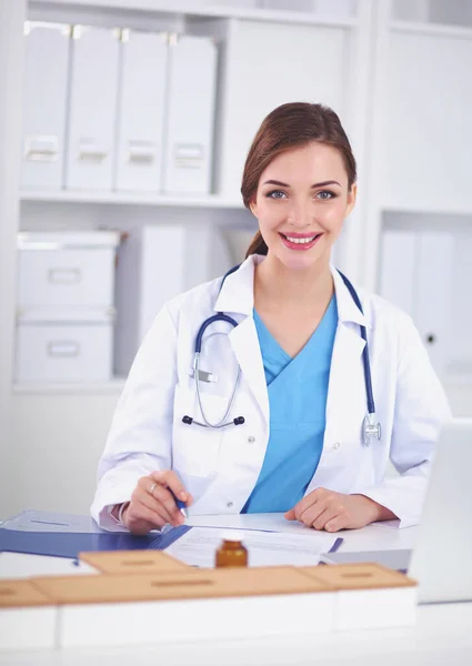 Bonito jovem sorridente médico feminino sentado na mesa e w — Fotografia de Stock