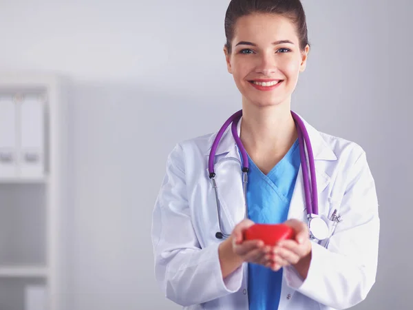 Ung kvinna läkare håller ett rött hjärta, stående på sjukhus — Stockfoto
