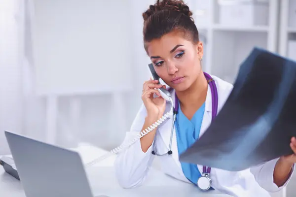 Ärztin sieht Röntgenbild und telefoniert im Diagnosezentrum, sitzt am Schreibtisch — Stockfoto