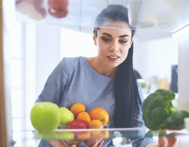 Gülümseyen kadın buzdolabından taze meyve alıyor, sağlıklı yiyecek konsepti.